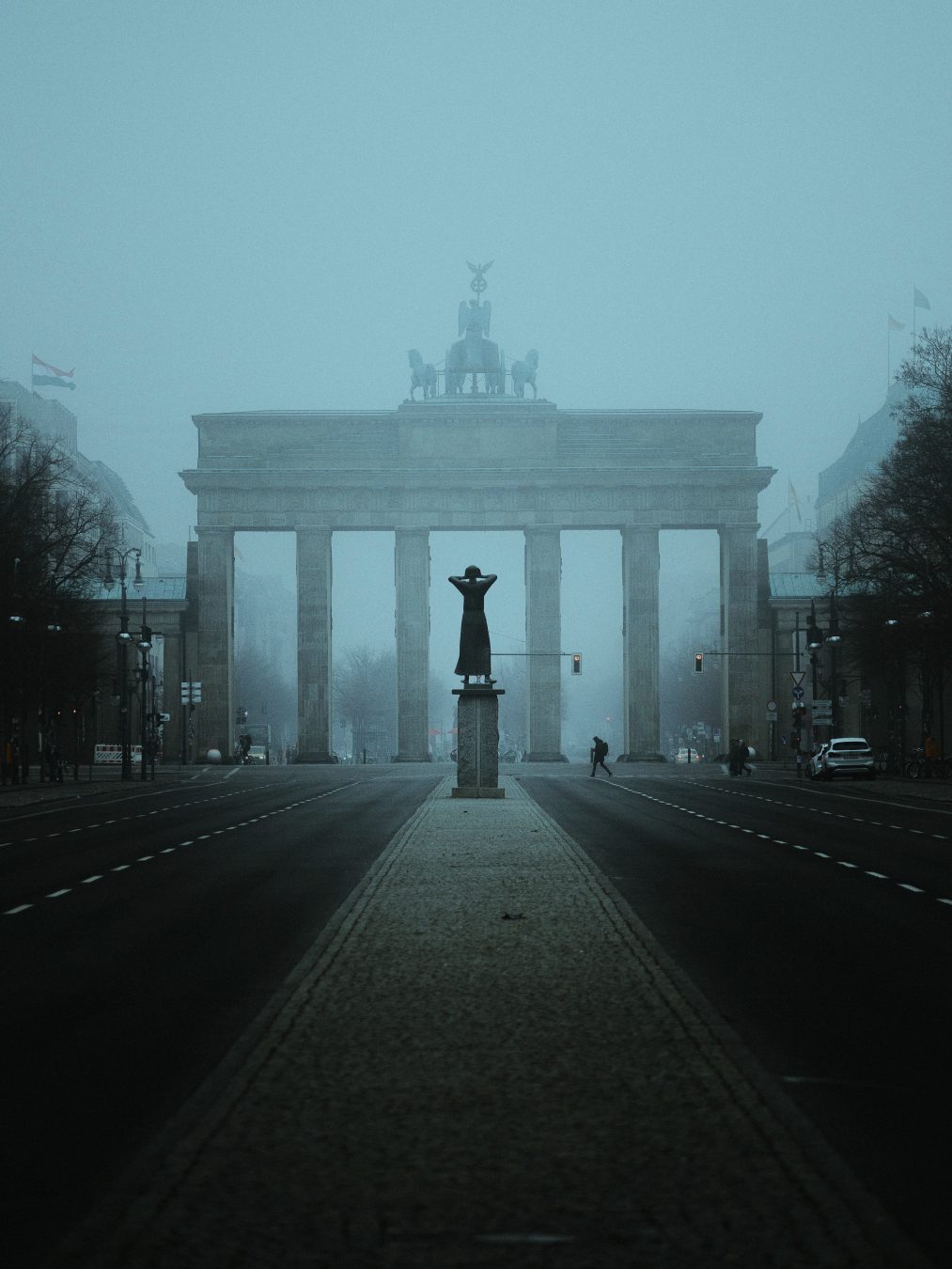 Brandenburg Gate almost erased by dense fog, a statue in the foreground, near-empty street