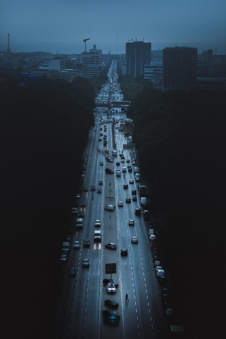 Elevated view of a dusk boulevard framed by dark tree canopies, one distant pedestrian