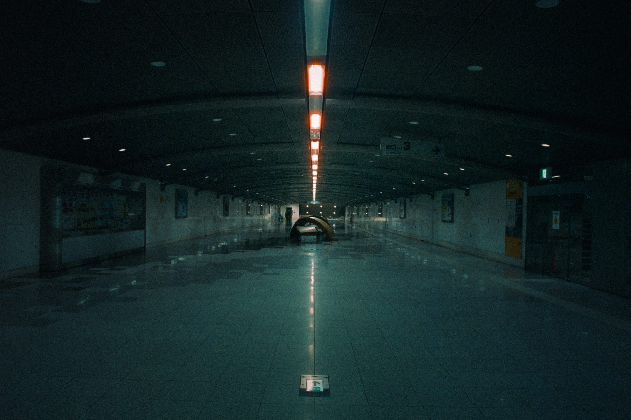 Empty underground station corridor at night, lit by a glowing overhead light strip