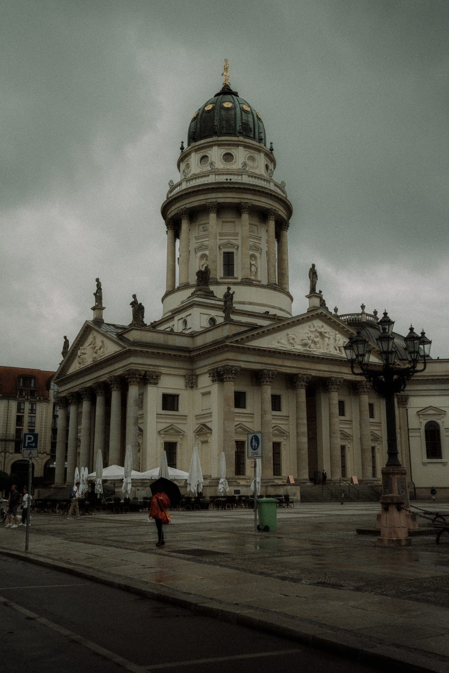 Deutscher Dom at Gendarmenmarkt on an overcast day, a figure in a red-orange jacket with a black umbrella in the foreground