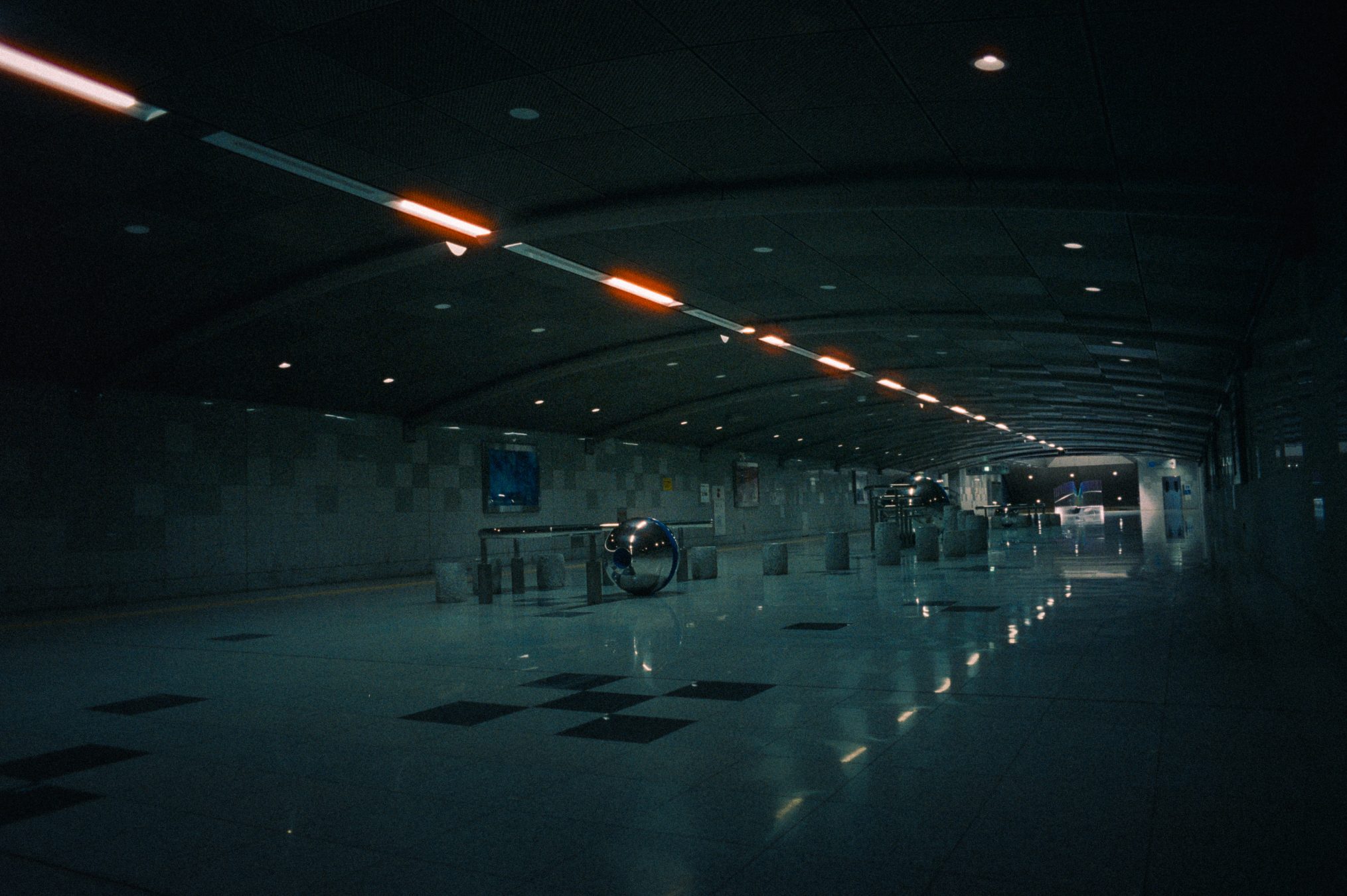 Underground station corridor at night with mirrored spherical sculptures and turnstile barriers
