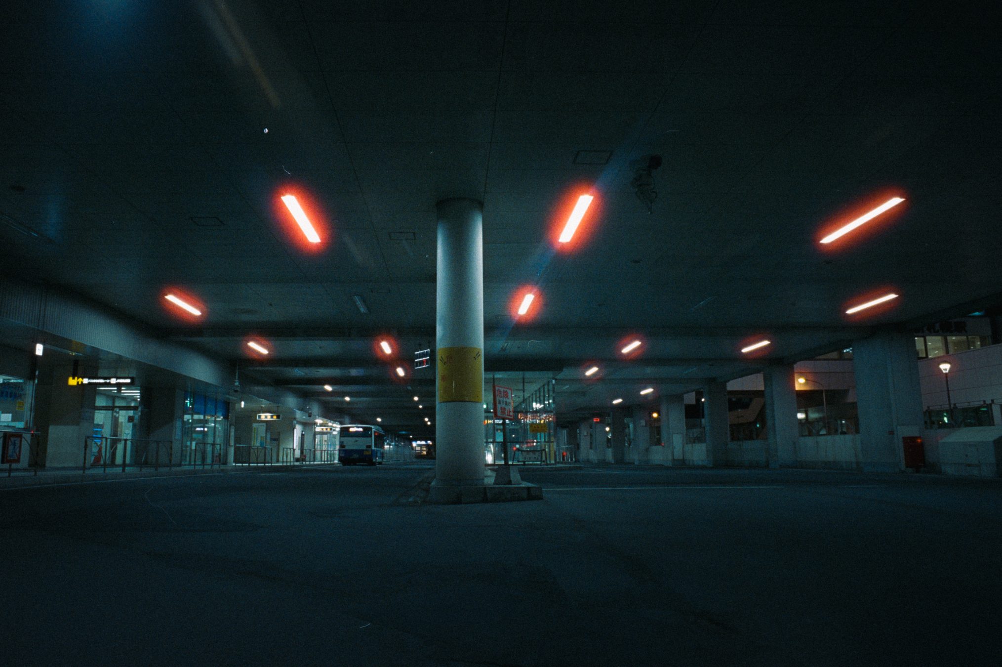 Covered bus terminal at night with a single bus parked under fluorescent lighting