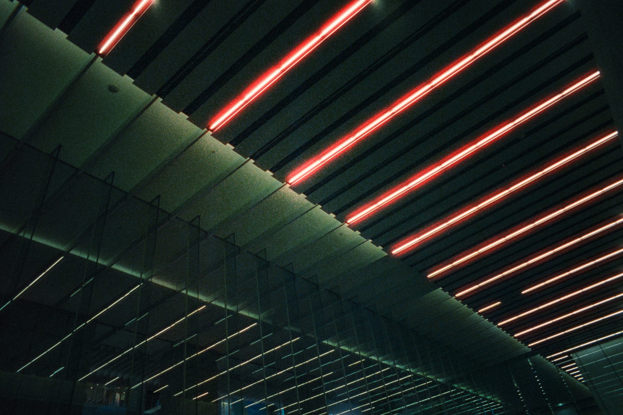 Architectural ceiling detail with diagonal red and white light strips reflected in glass
