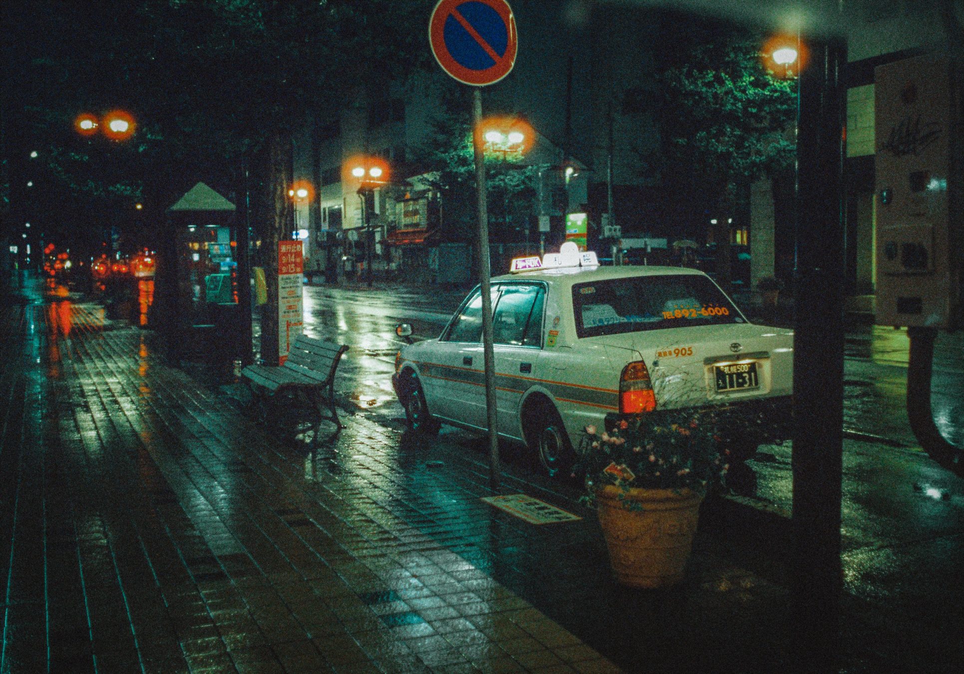 A Sapporo taxi parked on a rain-wet street at night