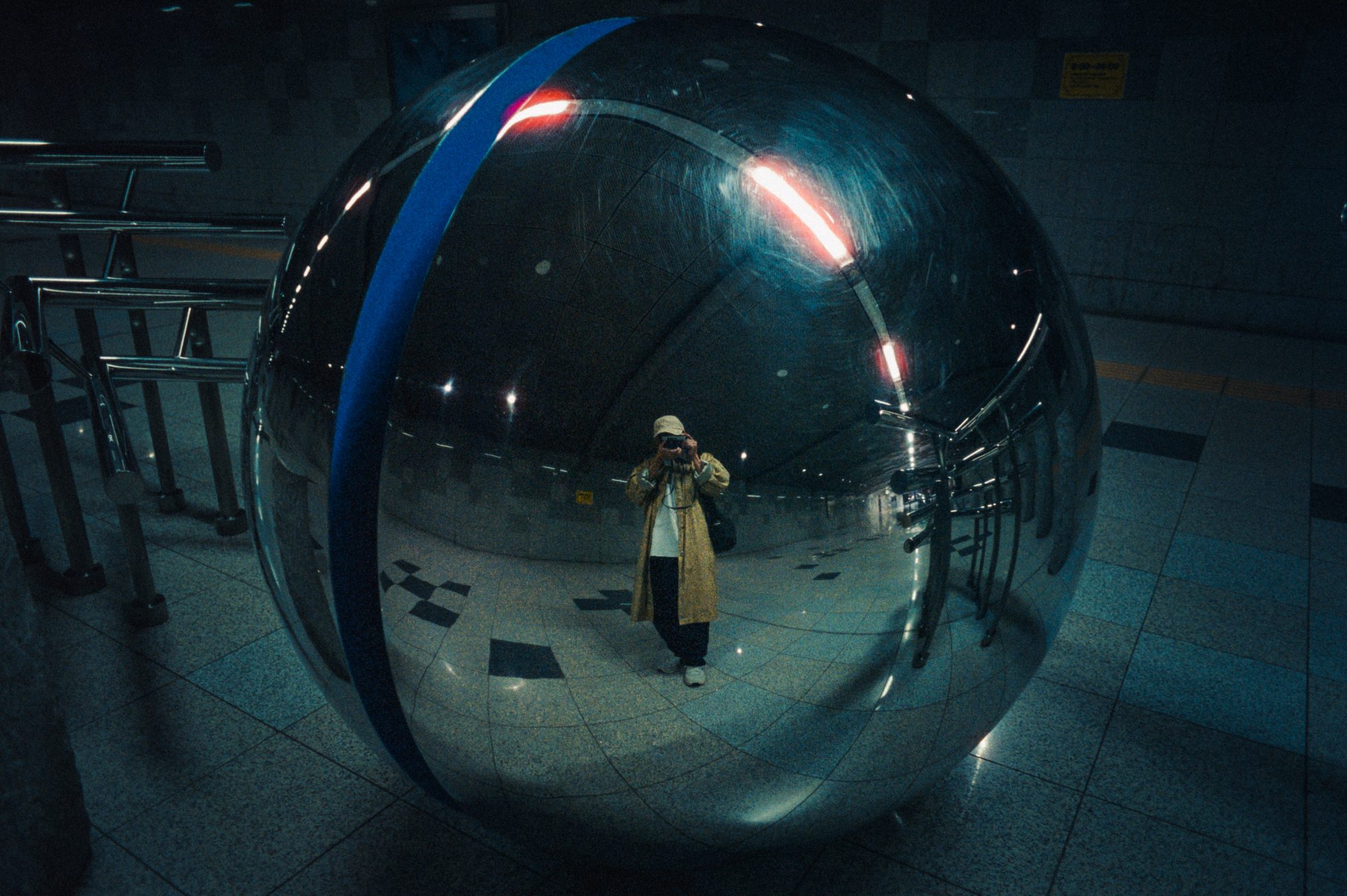 Self-portrait reflected in a mirrored sphere sculpture, camera raised to the face