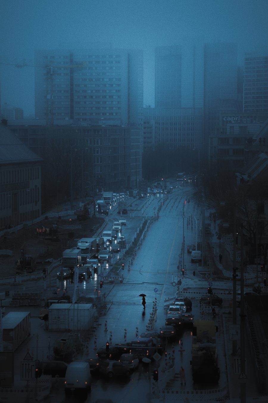 Foggy high-rise skyline with a solitary figure crossing an empty roadwork-lined street