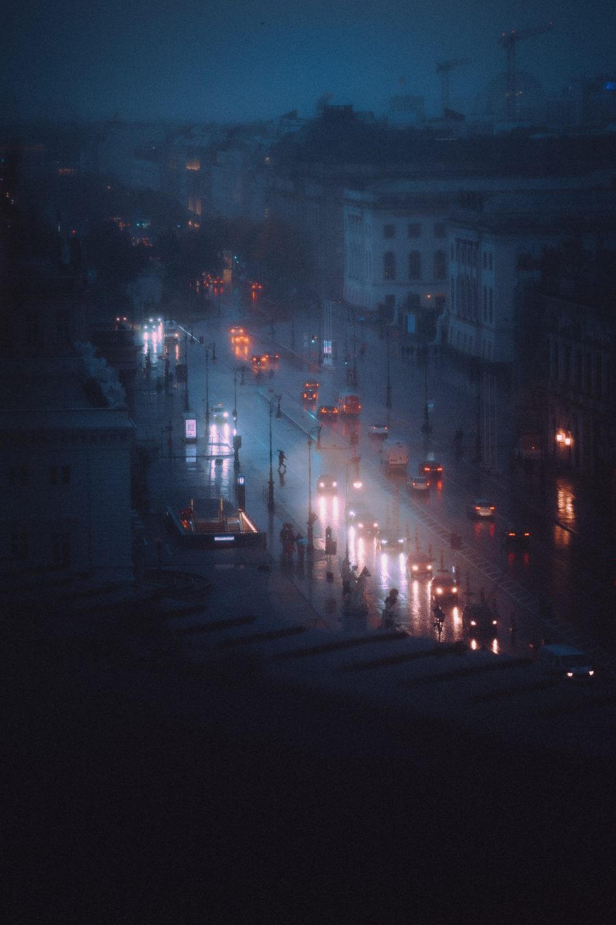 Elevated night view of a rainy Berlin street with glowing headlights and streetlights